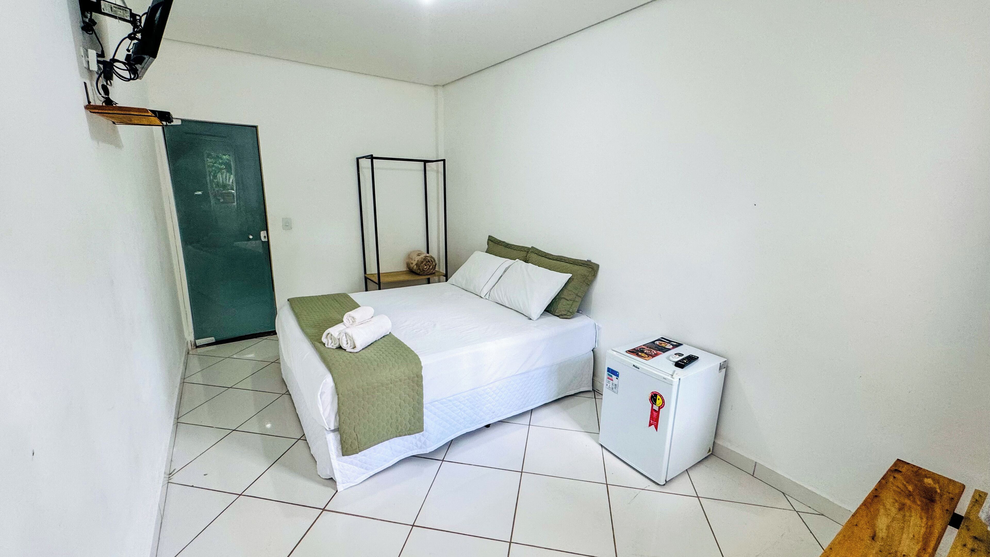 A hotel room with a bed, a small refrigerator, and a door.