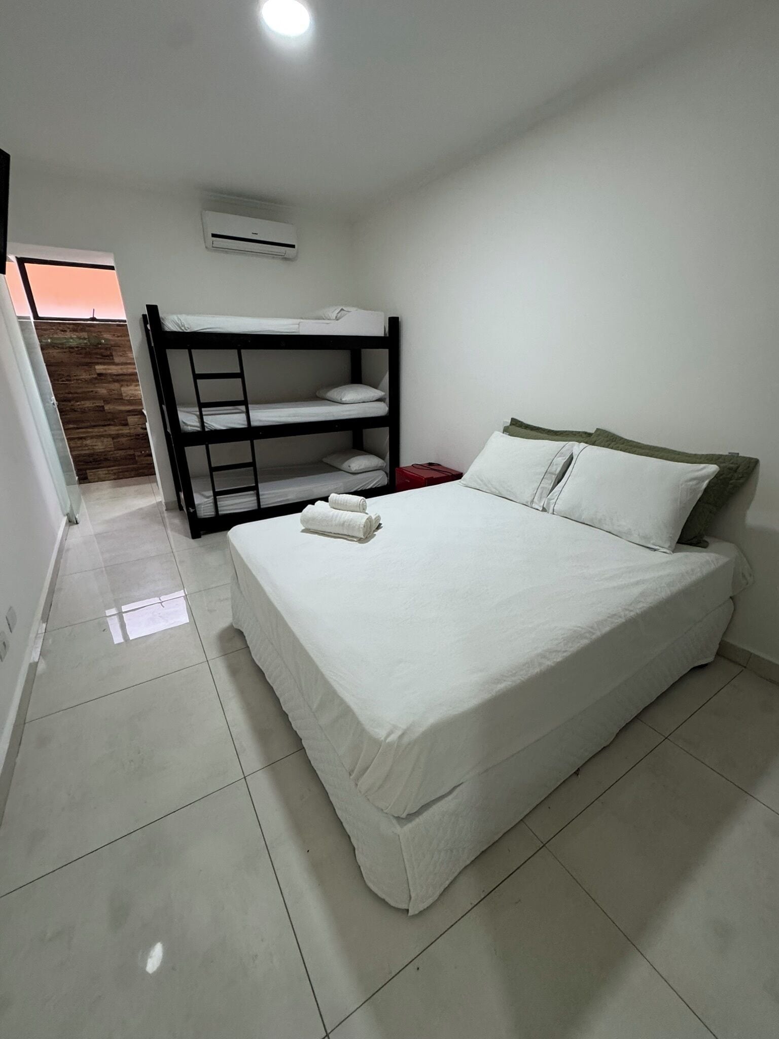 Een slaapkamer met een stapelbed, een enkel bed, wit beddengoed en een betegelde vloer.