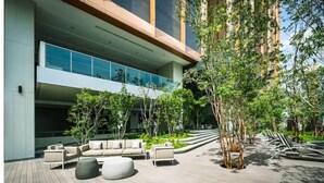 A modern outdoor lounge area with a wooden deck, seating arrangements, and a glass facade building in the background.