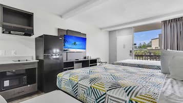 Habitación de hotel moderna con cama, televisión, microondas, refrigerador pequeño, escritorio y balcón con vistas.