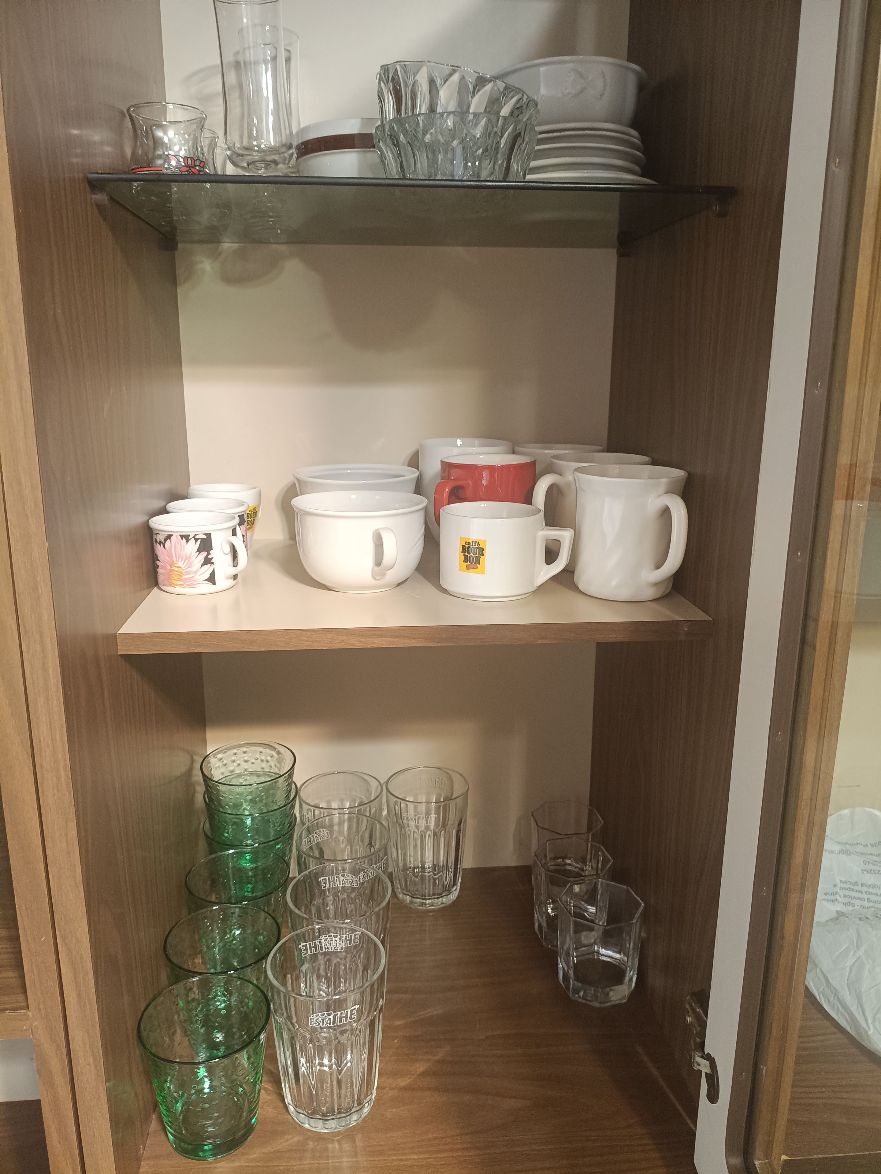 A shelf with various glassware and mugs, including a red mug with a sticker.