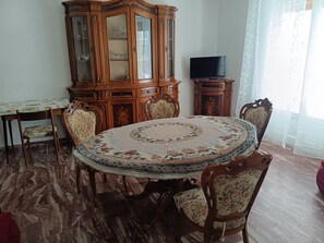 Une salle à manger avec une table ronde, des chaises, un buffet en bois et un téléviseur.