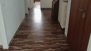 Un corridoio con pavimento in marmo, pareti bianche e una porta in legno.