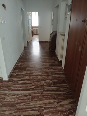 Un pasillo con piso de mármol, paredes blancas y una puerta de madera.