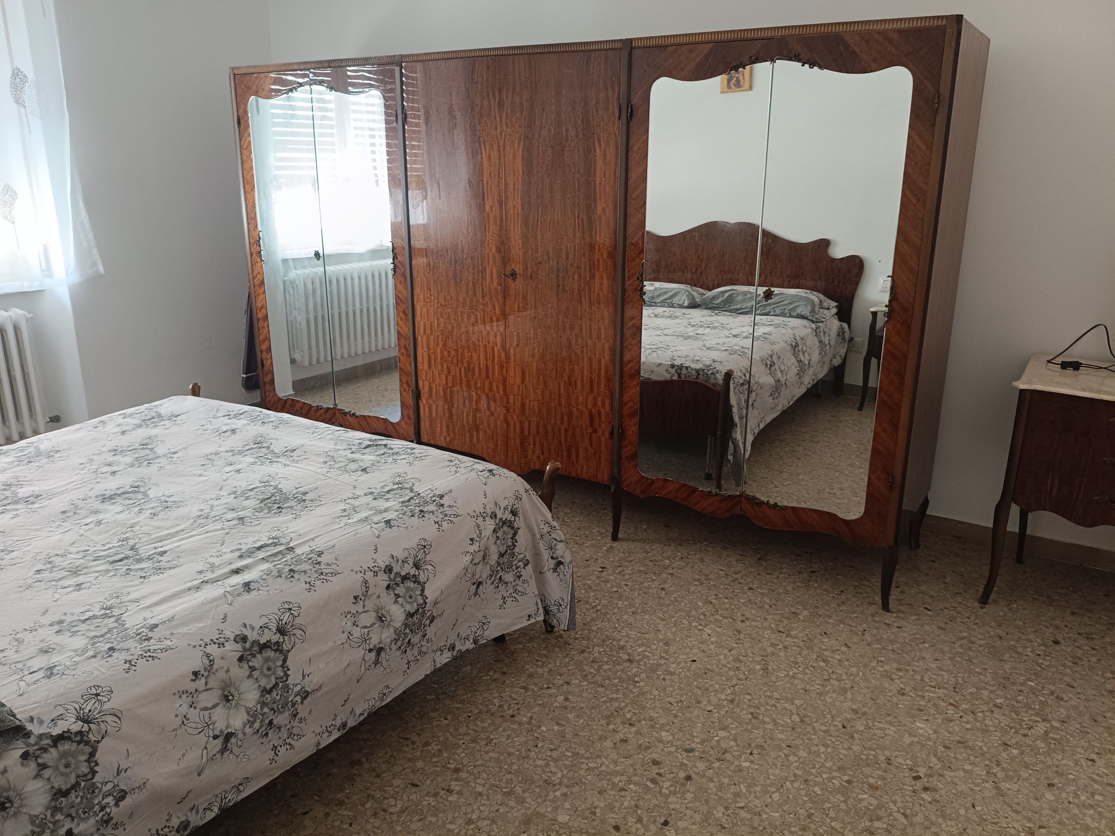 A bedroom with a bed, a wooden wardrobe, a mirror, and a radiator.