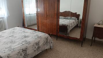 A bedroom with a bed, a wooden wardrobe, a mirror, and a radiator.