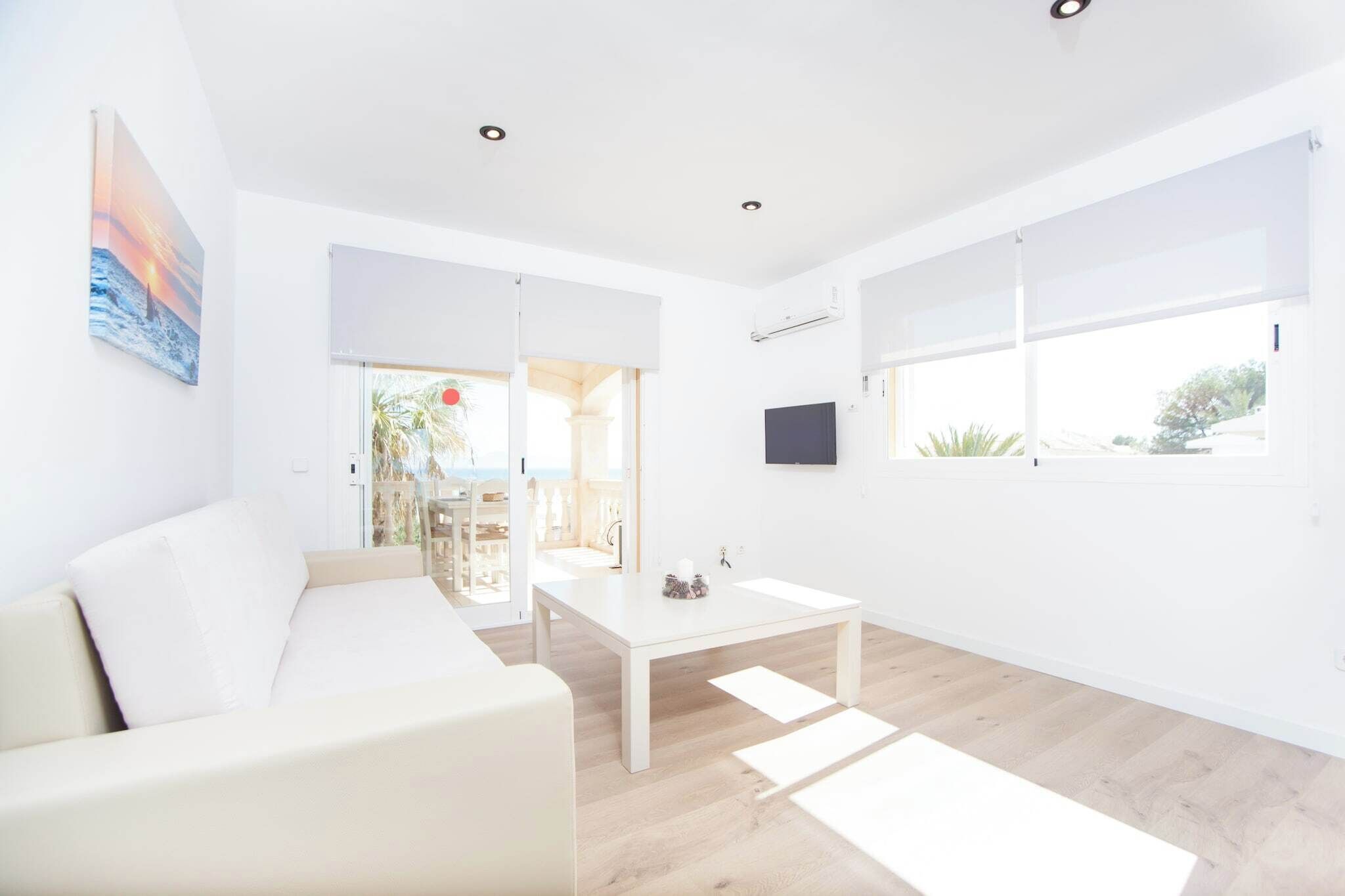 Un salón moderno y minimalista con un sofá blanco, una mesa de centro blanca y un ventanal grande que proporciona luz natural.