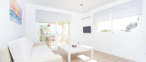 Un salón moderno y minimalista con un sofá blanco, una mesa de centro blanca y un ventanal grande que proporciona luz natural.