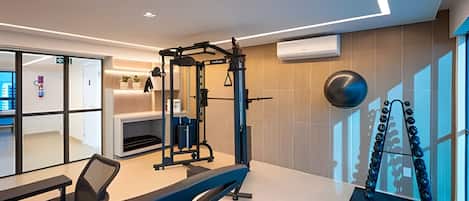 Un gimnasio moderno con equipamiento de ejercicio, una cinta de correr y un amplio ventanal que proporciona luz natural.