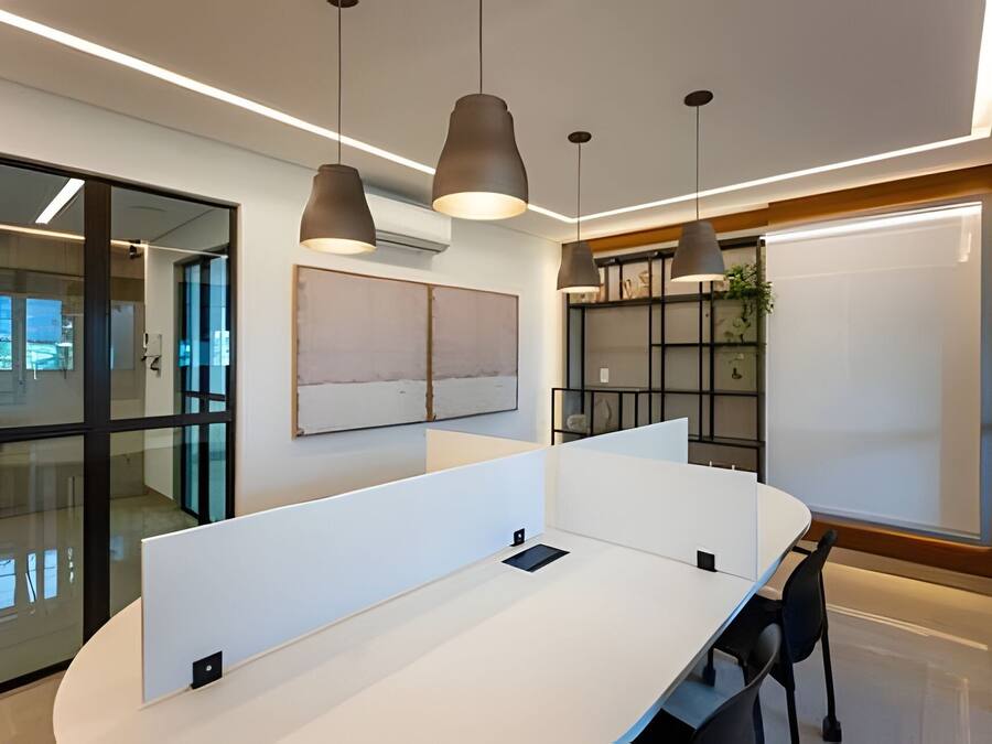 A modern office space with a white conference table, black chairs, pendant lighting, and a glass wall with a view.