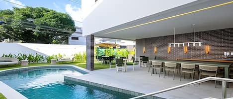 Un área de piscina exterior moderna con bar y asientos.