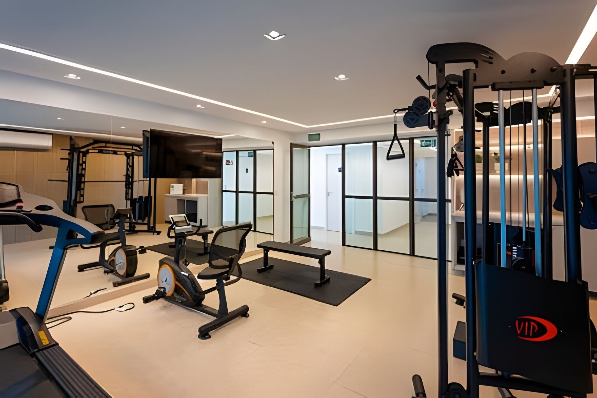 Un gimnasio moderno con máquinas de cardio, equipo de levantamiento de pesas y un espejo grande.