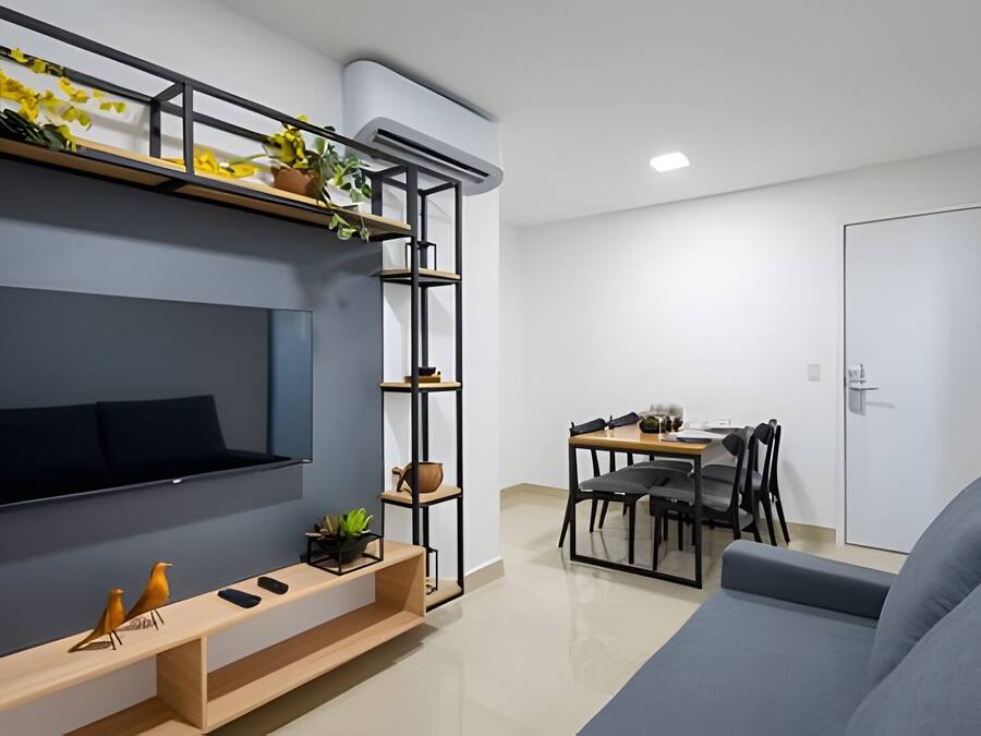 A modern living room with a flat-screen TV, wooden shelves, a sofa, and a dining area with chairs and a table.