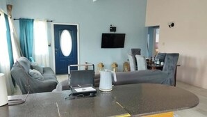 A living room with a curved coffee table, a sofa, a television mounted on the wall, and a door with an oval window. - FeeFee’s stay cation (Piggotts)