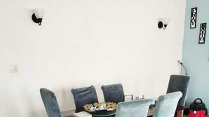 A dining area with a wooden table and six chairs, a small decorative bowl, and two wall-mounted light fixtures. - FeeFee’s stay cation (Piggotts)