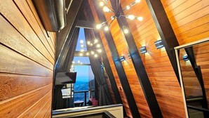 A sloped ceiling with wooden paneling and a modern chandelier. A red carpeted area leads to a balcony with a view. - Charms of the Friar Cottage (municipality of Bom Retiro)