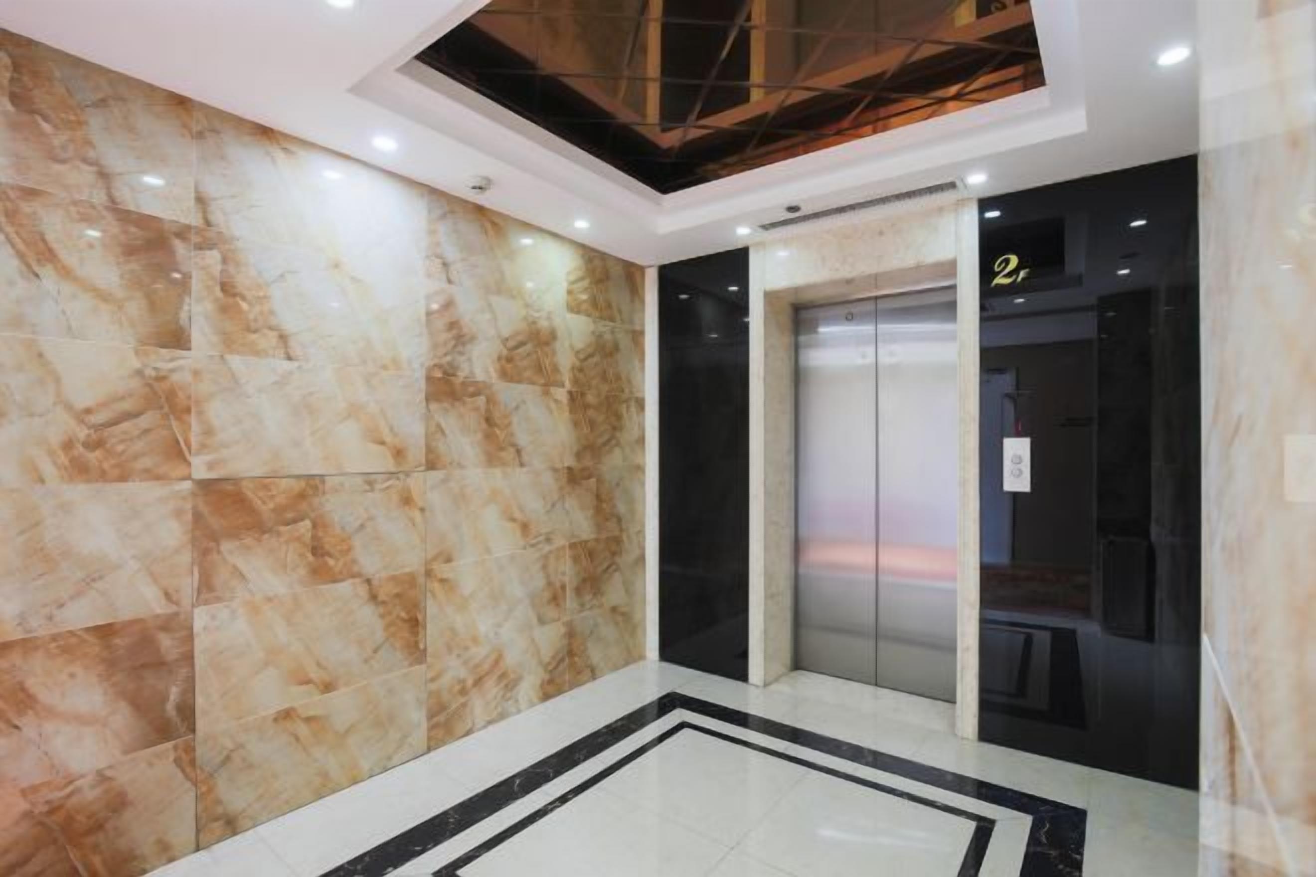 A modern elevator with a glass door, a marble wall, and a ceiling with recessed lighting.
