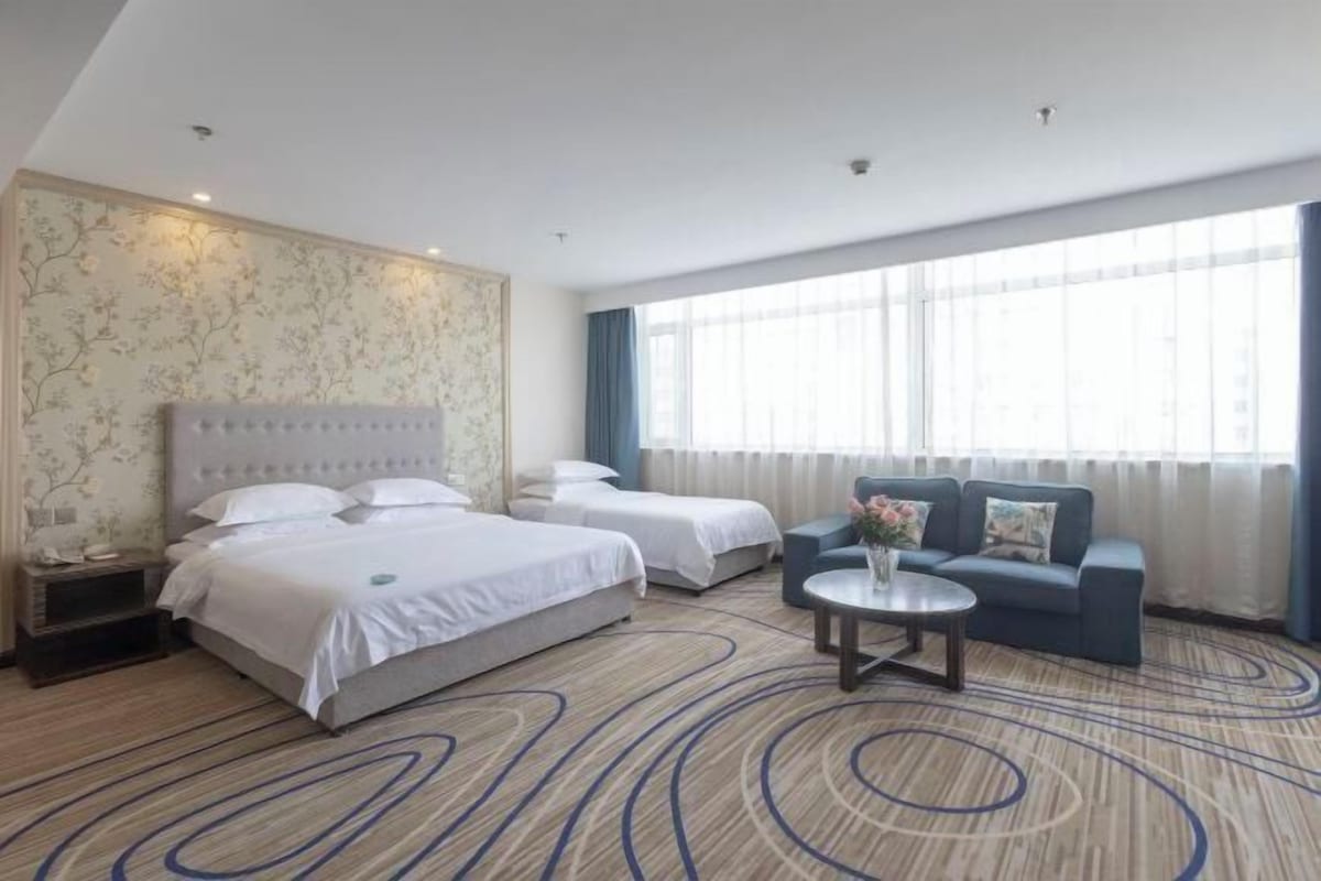 A hotel room with two beds, a sofa, a round coffee table, and a large window with curtains.