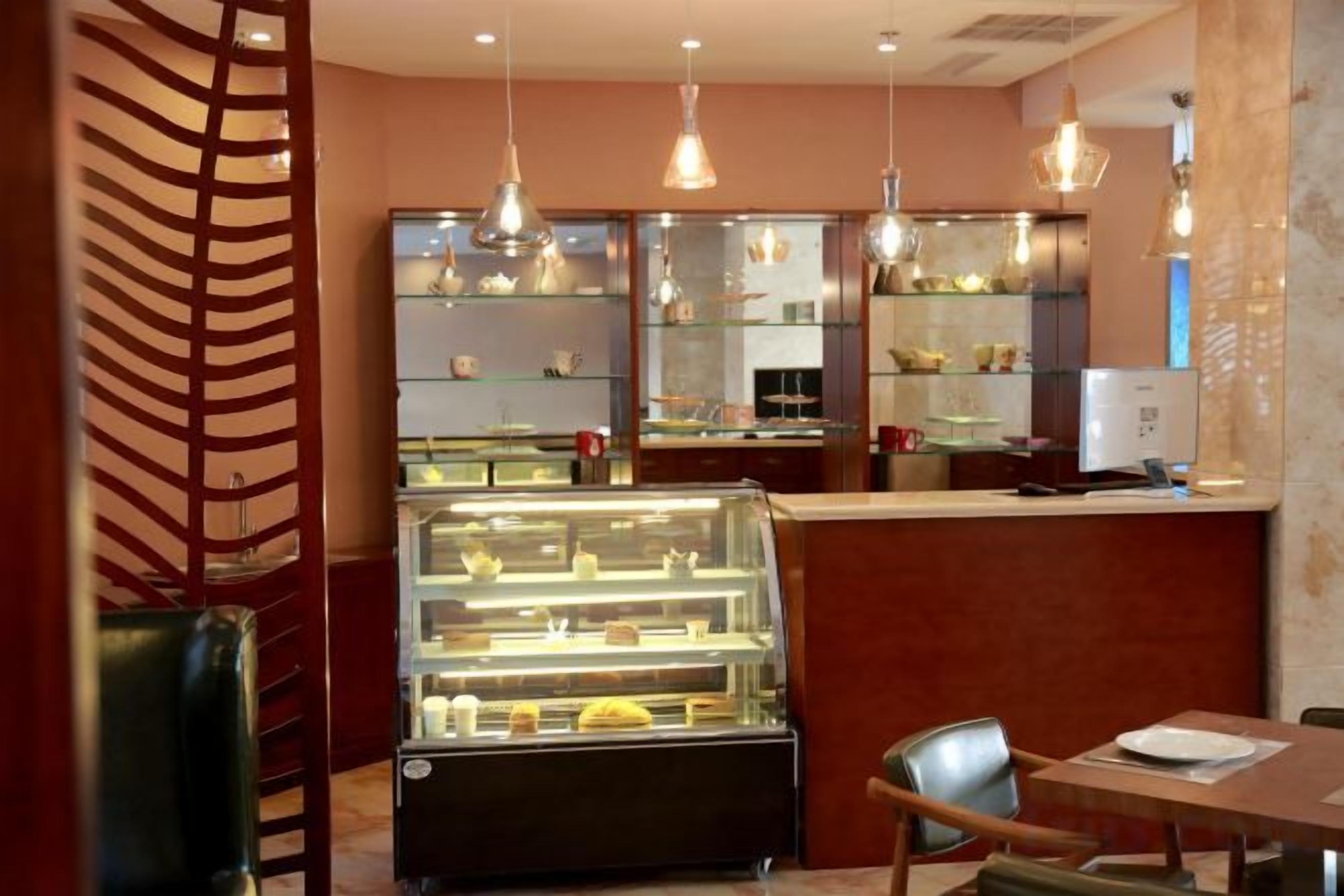 A restaurant interior with a counter, display case, hanging lights, and seating.