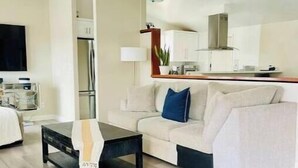 Una sala de estar moderna con un sofá, una mesa de centro y una cocina visible a través de un acceso abierto.