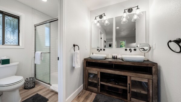 Een badkamer met twee wastafels, een douchecabine van glas en een houten wastafelmeubel.