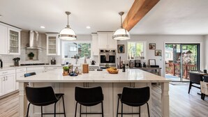 A modern kitchen with white cabinetry, a large island with bar stools, stainless steel appliances, and pendant lighting. - Geraldine Drive by Avantstay Hot Tub, Views, Walk to Trails + Game Room (Incline Village)