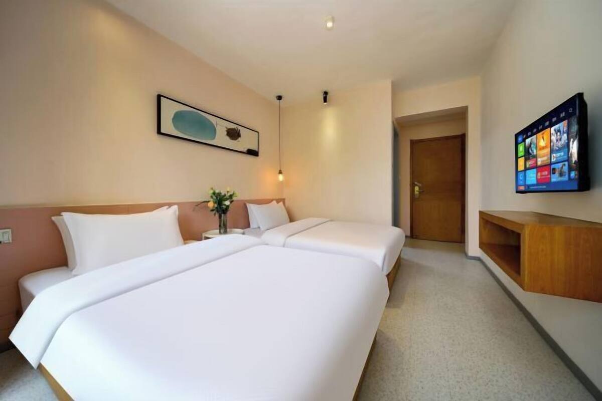 Habitación de hotel con dos camas, un televisor montado en la pared, un armario de madera y una puerta que da a otra habitación.