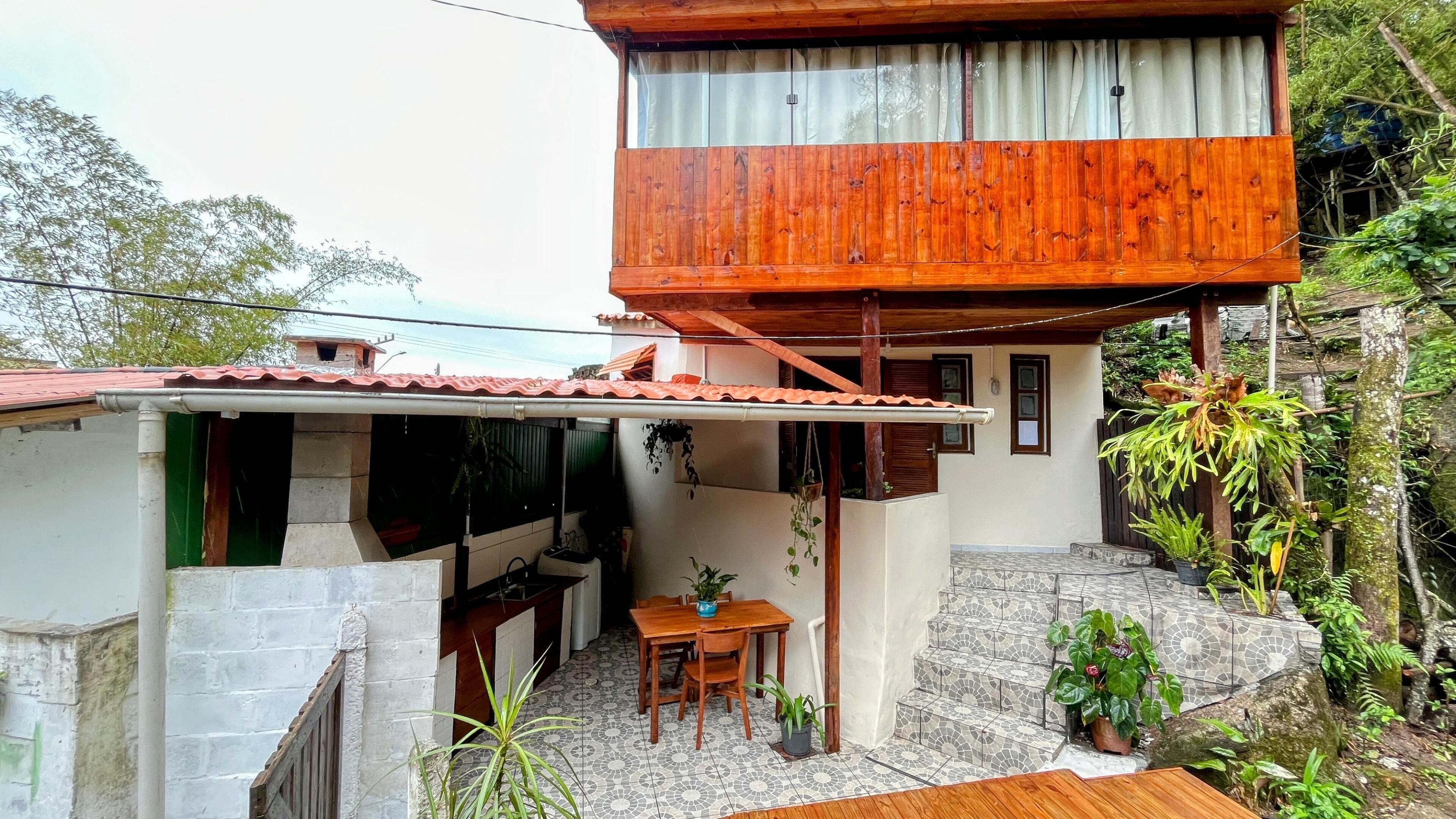 Una casa a due piani con un balcone in legno, un patio piastrellato e un piccolo spazio pranzo.