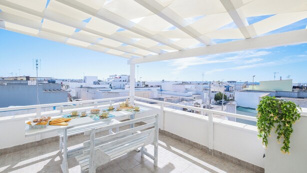 A rooftop terrace with a white pergola, a table with food items, and a hanging plant.