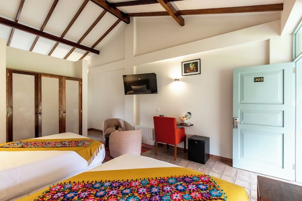A hotel room with two beds, a desk, a chair, a TV, and a door with the number 303. - Hotel Casa Eva (Urubamba)