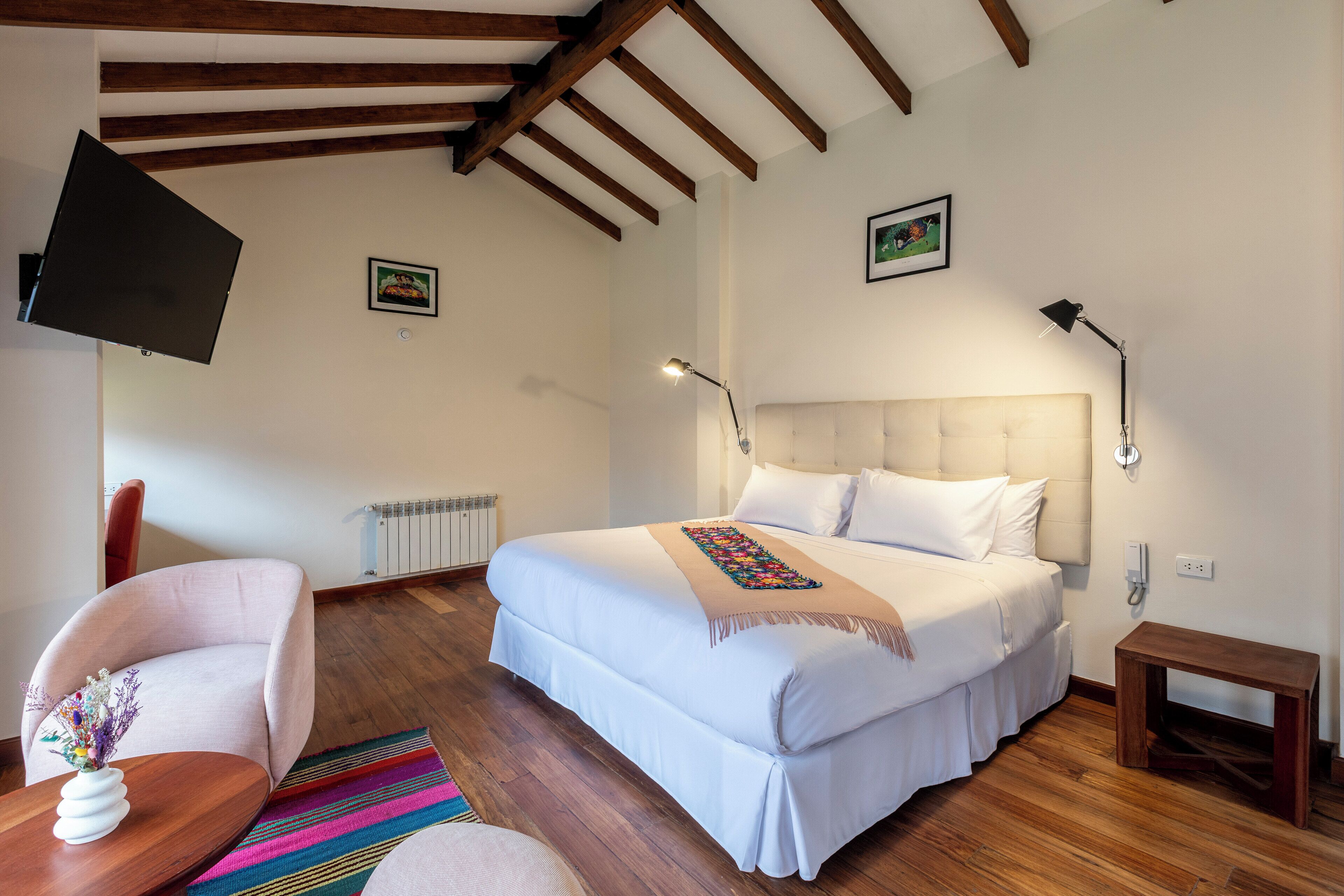 Quarto com uma cama grande, uma cadeira, uma mesinha, uma televisão e um abajur.