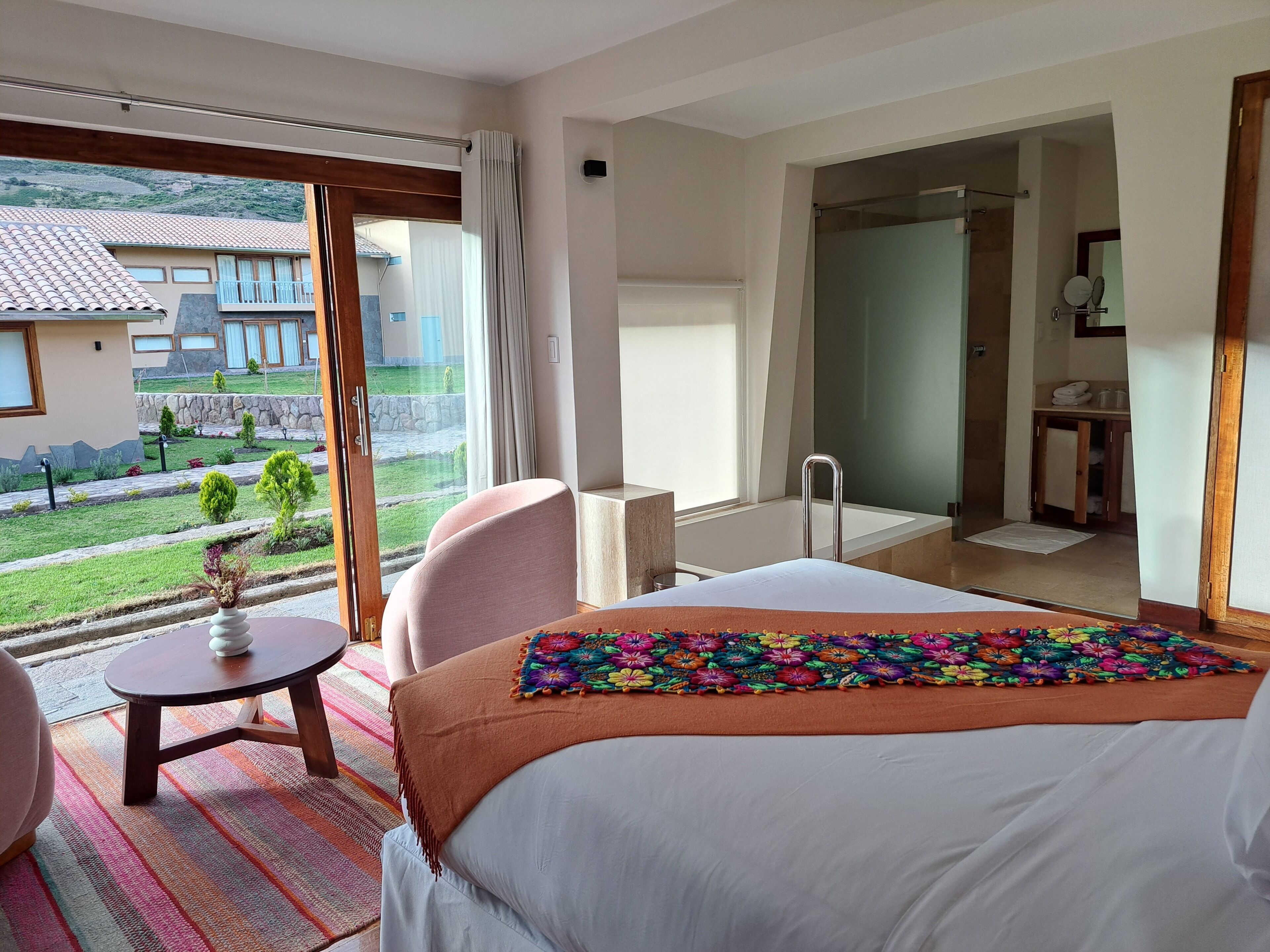 A hotel room with a large bed, a small table, a chair, and a view of the outside.