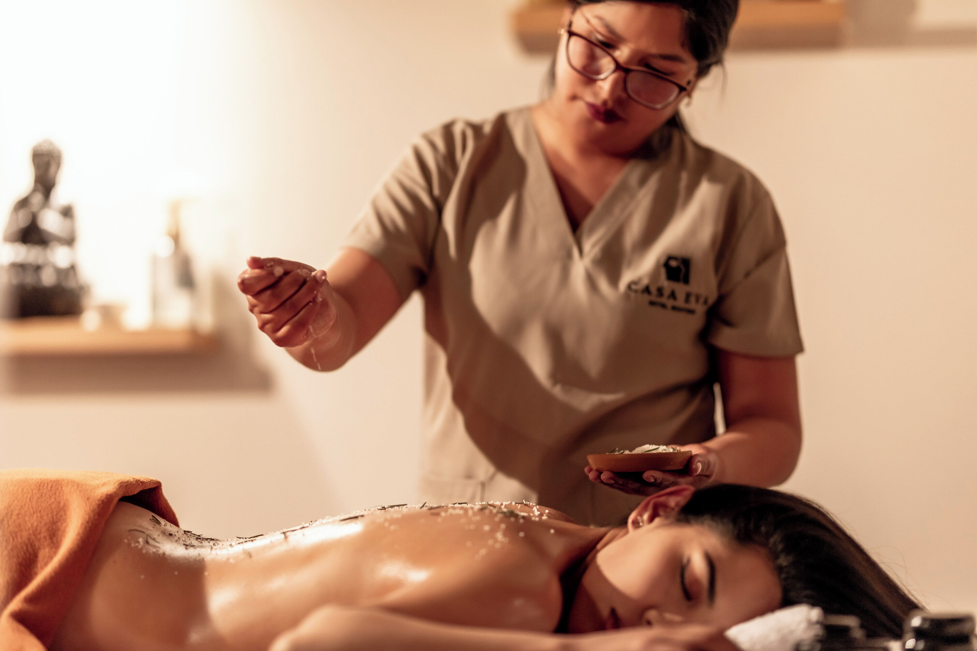 A person receiving a massage in a room with a statue and a shelf in the background.