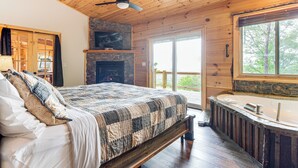 Ein Schlafzimmer mit einem großen Bett, einem Kamin aus Stein, einer Holzbalkendecke und Blick ins Freie.