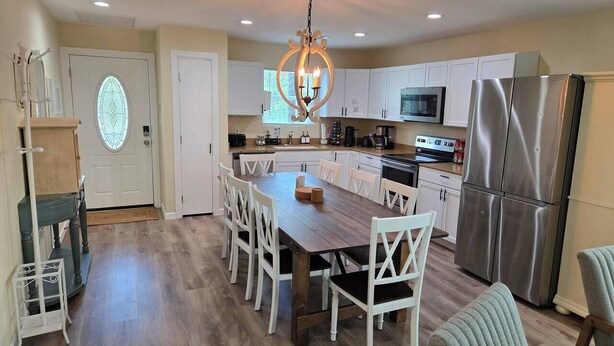 A spacious kitchen with white cabinets, a stainless steel refrigerator, and a wooden dining table with white chairs.