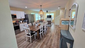 A modern kitchen with white cabinets, a dining area with a wooden table and chairs, and a built-in TV.