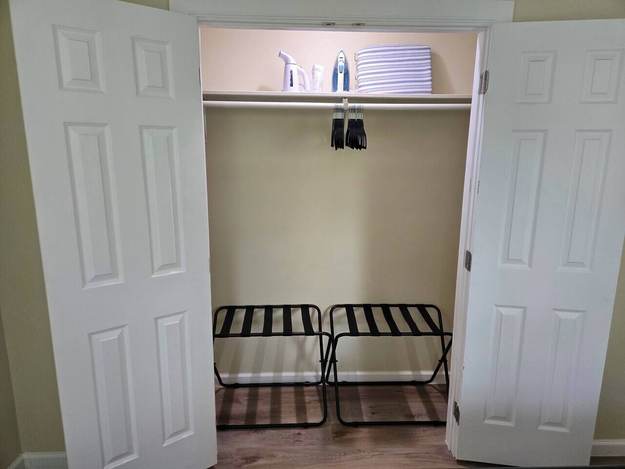 Un placard dont la porte est ouverte, révélant des étagères avec des vêtements pliés, une tringle à vêtements et une paire de chaises à rayures noires et blanches.