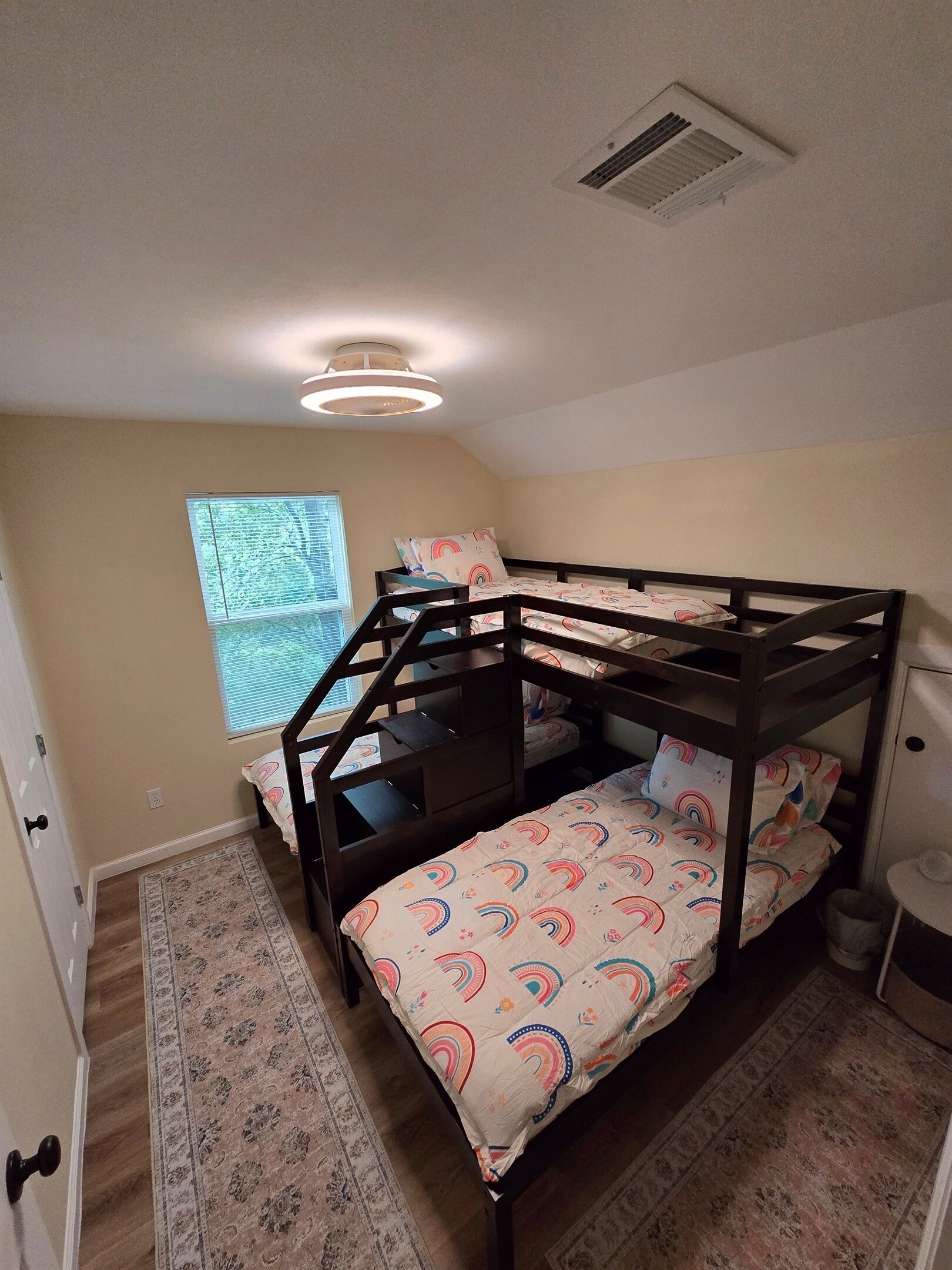 A bunk bed room with a patterned bedspread, a window with blinds, a ceiling vent, and a rug on the floor.