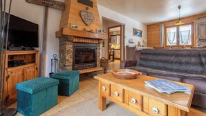 A cozy living room with a stone fireplace, wooden furniture, and a television. - Chalet Laura, Ski & Authenticity (Les Belleville)