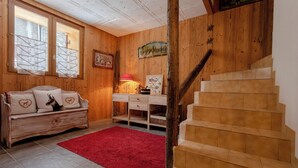 A wooden interior with a staircase, a red rug, a wooden sofa with decorative pillows, and a desk with a lamp. - Chalet Laura, Ski & Authenticity (Les Belleville)
