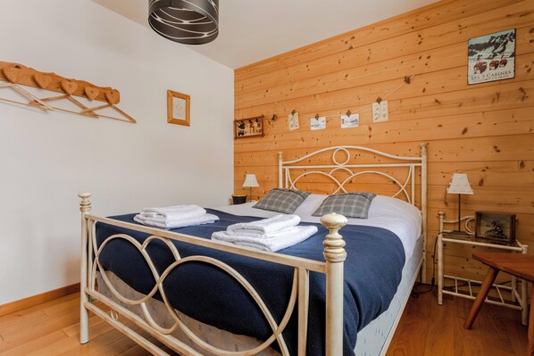 A neatly made bed with a blue blanket and white linens, a wooden headboard, and a wooden wall with a mounted picture. - Chalet Laura, Ski & Authenticity (Les Belleville)