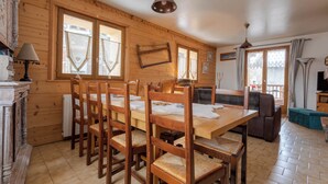 A wooden interior with a dining table, chairs, a sofa, and a television. - Chalet Laura, Ski & Authenticity (Les Belleville)