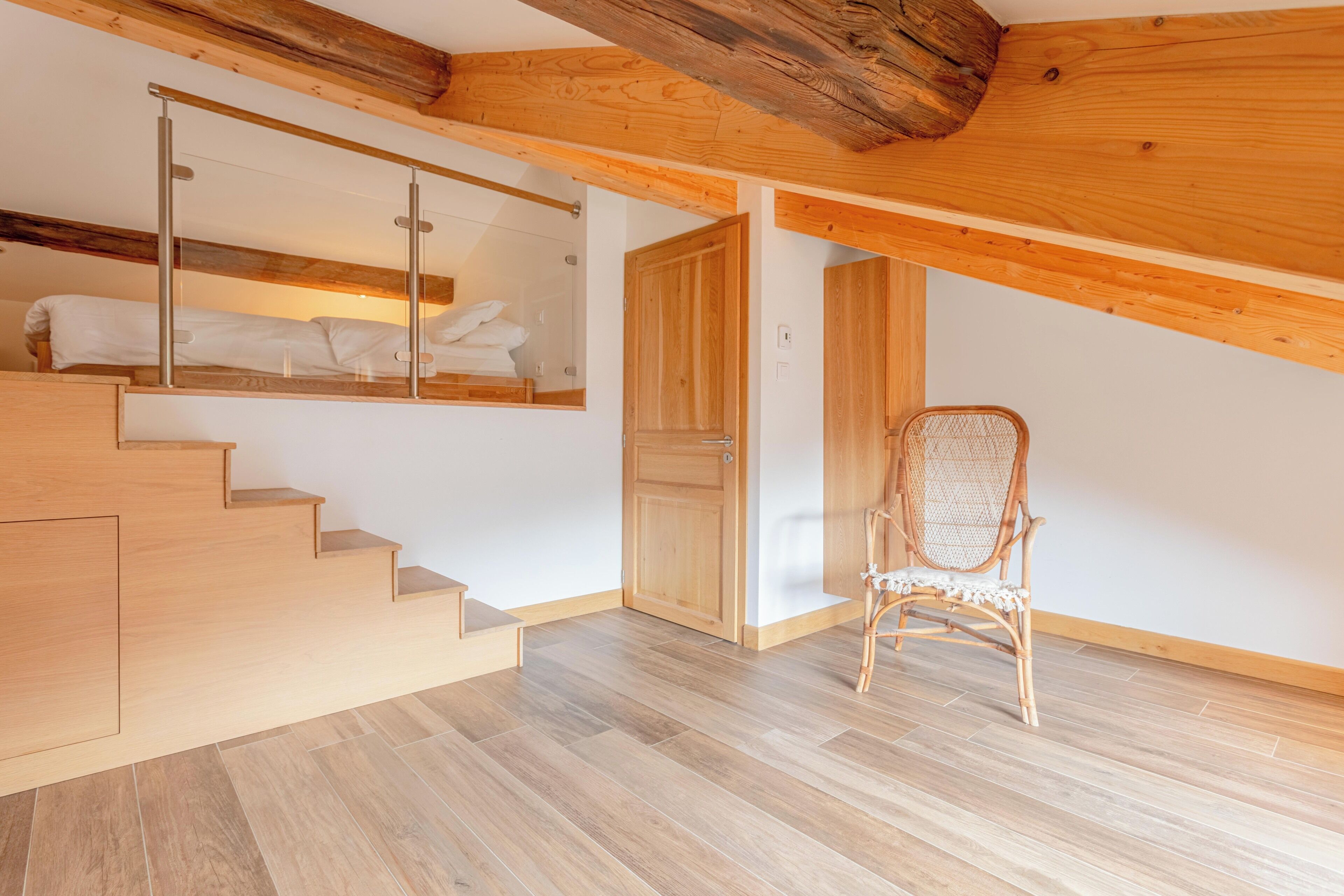 A wooden staircase leading to a loft bedroom with a bed and a mirror.