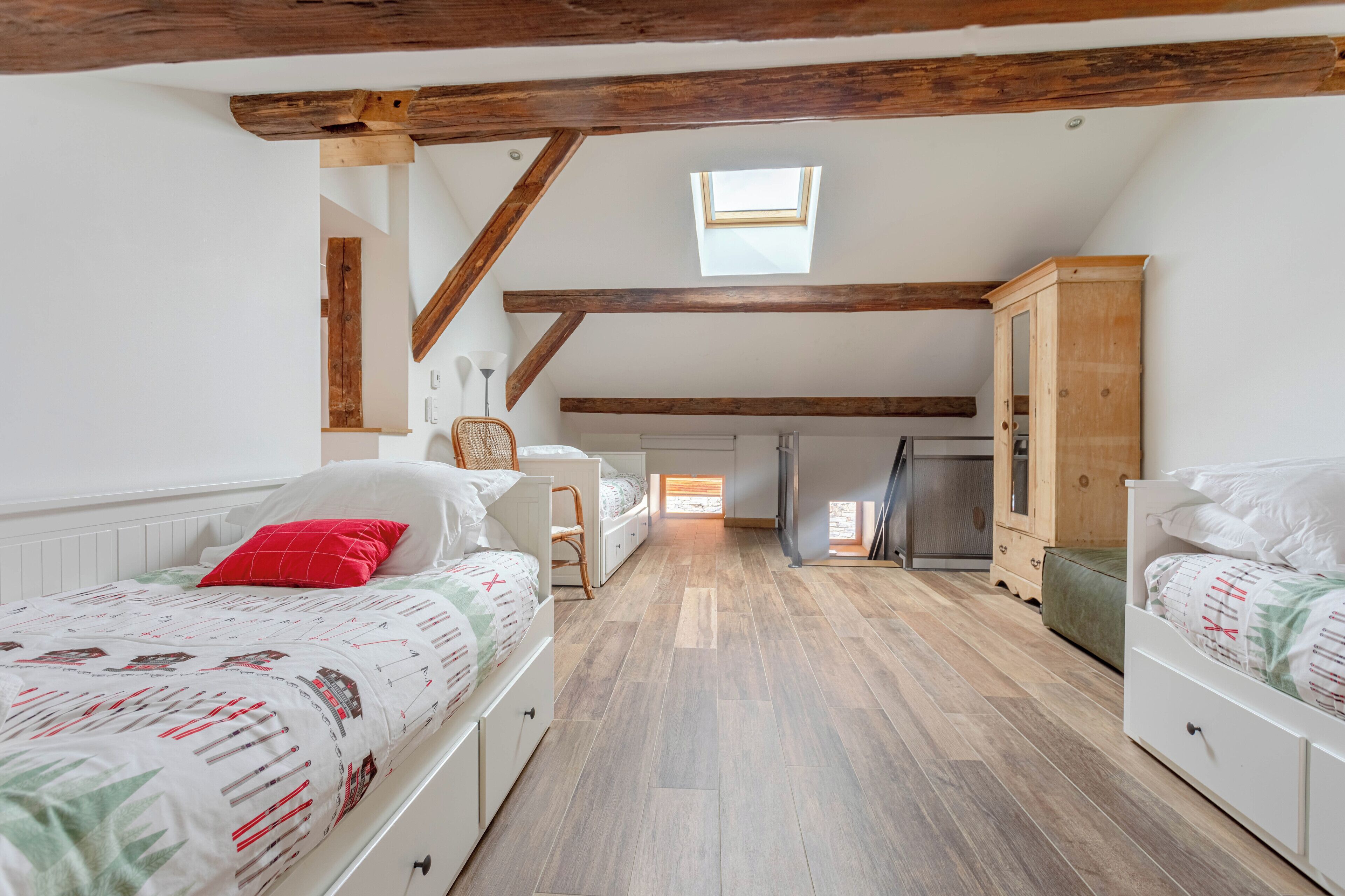 Un dormitorio con dos camas, un tragaluz, vigas de madera, un armario y una pequeña cocina americana.