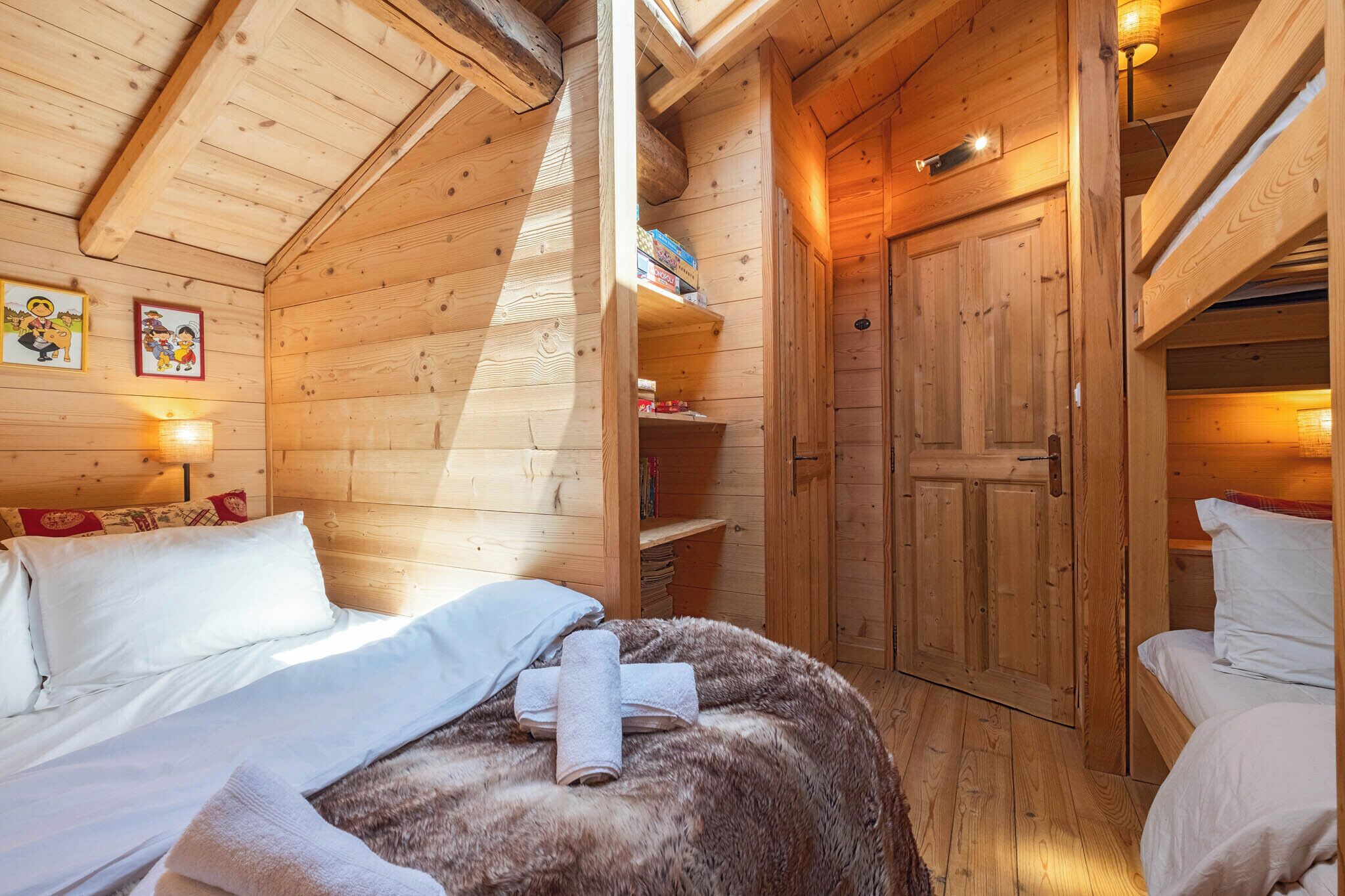 A cozy wooden cabin room with a bed, a small shelf with books, and a wardrobe.