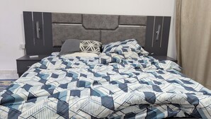 Een bed met een beddengoed met een geometrisch patroon, een grijs bekleed hoofdbord en een nachtkastje met een afstandsbediening.