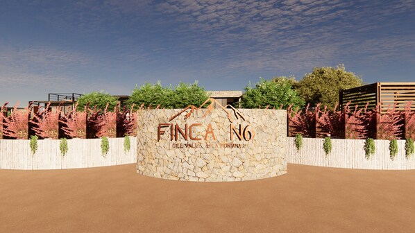 A stone wall with the text "FINCA No del Valle La Montana" and a wooden fence with red flowering plants.