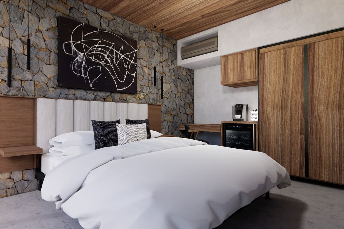 Une chambre avec un mur en pierre, un lit avec une literie blanche, une tête de lit en bois et une machine à café.
