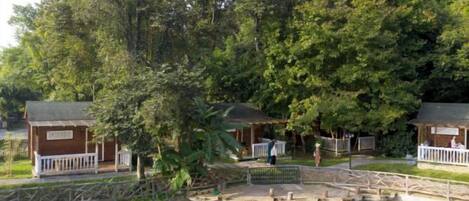 A wooden cabin-style building with a porch, a small bridge over a pond, and dense surrounding trees.