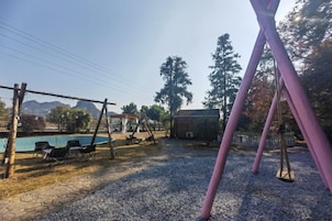 Un parque infantil con columpios y una piscina al fondo.